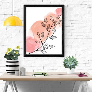 May include: A black framed print with a watercolor background in shades of pink and a black line drawing of a branch with leaves.