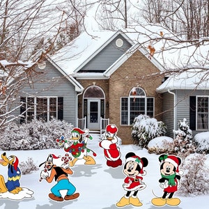May include: A snowy winter scene with a house in the background and various Christmas-themed decorations of Mickey Mouse and his friends. The decorations include Mickey Mouse, Minnie Mouse, Goofy, Donald Duck, and Pluto.