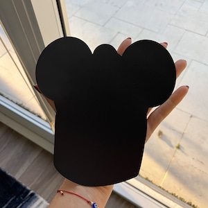 May include: Black silhouette of a chef's hat with two rounded ears on top, held in a person's hand.