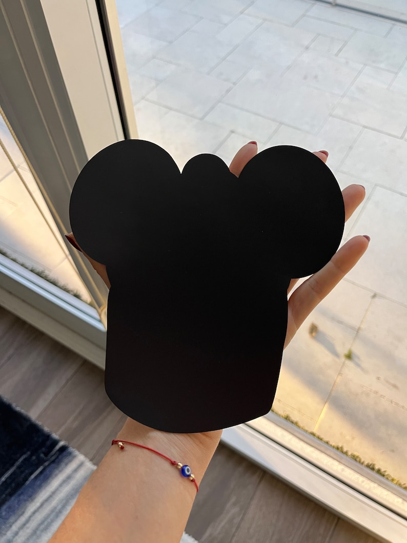 May include: Black silhouette of a chef's hat with two rounded ears on top, held in a person's hand.