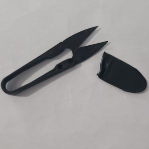 May include: Black thread snips with a curved handle and pointed blades, alongside a matching protective cover. The scissors are designed for precision cutting in sewing and crafting projects.