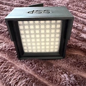 May include: A black box with a grid of white lights and the word "dss" printed on the top.