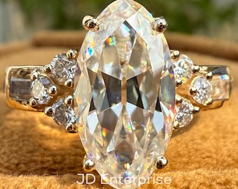 Puede incluir: Un anillo de oro con un gran diamante de forma ovalada y diamantes más pequeños engastados a su alrededor. El anillo está sobre una superficie de terciopelo marrón.