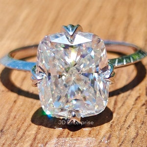 Peut inclure: Une bague en argent avec un grand diamant taille coussin clair. Le diamant est serti à griffes avec quatre griffes. La bande de la bague est fine et a une finition texturée.