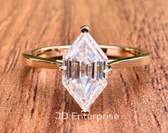 May include: A gold ring with a clear, kite-shaped diamond. The ring is on a wooden surface. JD Enterprise