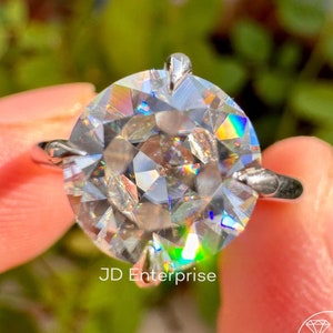 Puede incluir: Primer plano de un anillo de plata con una gran piedra preciosa redonda, clara y facetada. La piedra preciosa tiene un efecto arcoíris. El anillo está en un dedo.