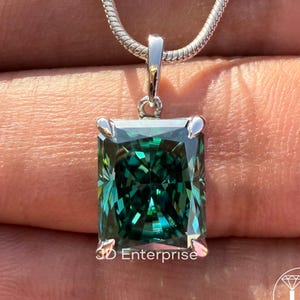 May include: A silver pendant necklace featuring a large, emerald-cut, teal-colored gemstone. The gemstone is set in a silver bezel and hangs from a delicate silver chain. The text "3D Enterprise" is visible on the pendant.