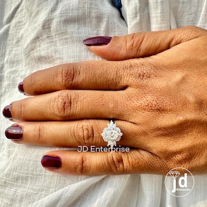 May include: A silver engagement ring with a large oval-shaped center stone surrounded by smaller diamonds. The ring is set in a halo style with a delicate band.