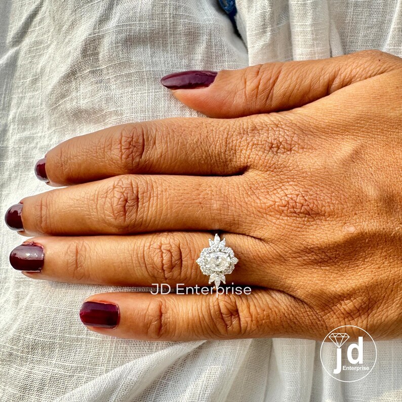 May include: A silver engagement ring with a large oval-shaped center stone surrounded by smaller diamonds. The ring is set in a halo style with a delicate band.