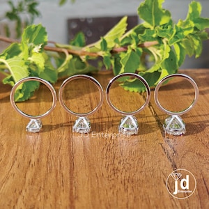 Puede incluir: Cuatro anillos de plata con piedras redondas transparentes engastadas en el centro. Los anillos se muestran sobre una superficie de madera.