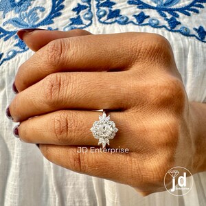 May include: A silver ring with a large oval-shaped center stone surrounded by smaller diamonds. The ring is set in a halo style with a delicate band.