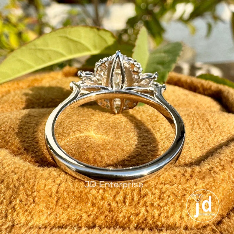 May include: A silver ring with a large, clear, oval-shaped center stone surrounded by smaller, clear stones. The ring is on a brown velvet surface.