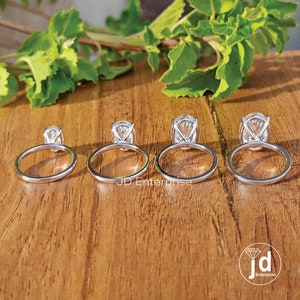 Puede incluir: Cuatro anillos de compromiso de plata con diamantes de forma ovalada. Los anillos est&aacute;n dispuestos en una fila del m&aacute;s peque&ntilde;o al m&aacute;s grande. Los anillos est&aacute;n sobre una superficie de madera.