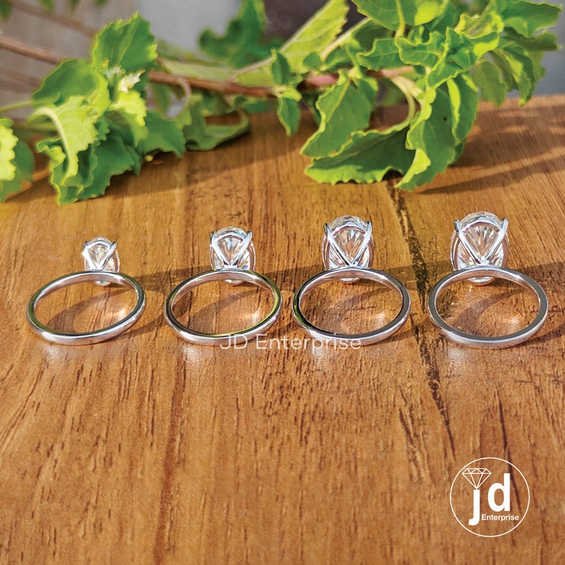 Puede incluir: Cuatro anillos de compromiso de plata con diamantes de forma ovalada. Los anillos est&aacute;n dispuestos en una fila del m&aacute;s peque&ntilde;o al m&aacute;s grande. Los anillos est&aacute;n sobre una superficie de madera.