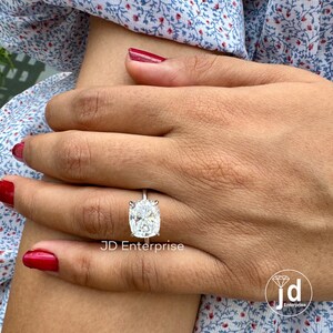 May include: A silver ring with a large, oval-shaped, clear gemstone. The ring is on a person's finger. The text "JD Enterprise" is visible below the ring.