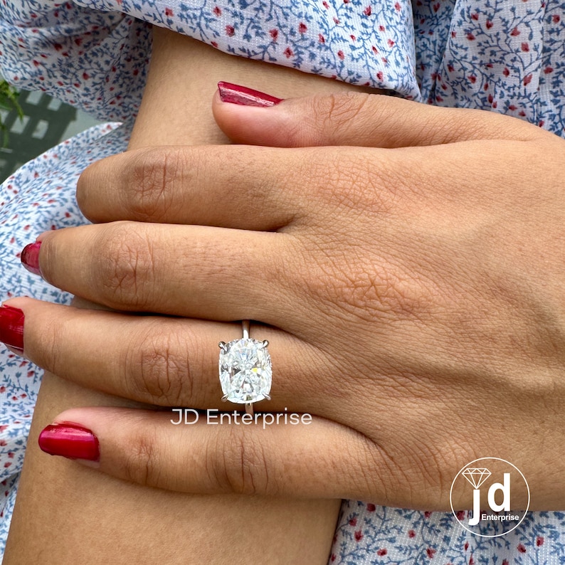 May include: A silver ring with a large, oval-shaped, clear gemstone. The ring is on a person's finger. The text "JD Enterprise" is visible below the ring.