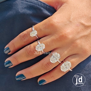 Puede incluir: Cuatro anillos de compromiso de diamantes de forma ovalada de diferentes tama&ntilde;os en una mano. Los anillos est&aacute;n engastados en plata y tienen un dise&ntilde;o cl&aacute;sico. El anillo m&aacute;s grande est&aacute; en el dedo me&ntilde;ique, y el anillo m&aacute;s peque&ntilde;o est&aacute; en el dedo &iacute;ndice. Todos los anillos est&aacute;n engastados en garras.