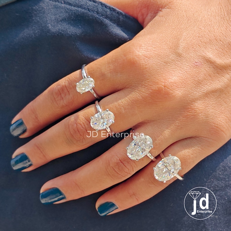 Puede incluir: Cuatro anillos de compromiso de diamantes de forma ovalada de diferentes tama&ntilde;os en una mano. Los anillos est&aacute;n engastados en plata y tienen un dise&ntilde;o cl&aacute;sico. El anillo m&aacute;s grande est&aacute; en el dedo me&ntilde;ique, y el anillo m&aacute;s peque&ntilde;o est&aacute; en el dedo &iacute;ndice. Todos los anillos est&aacute;n engastados en garras.