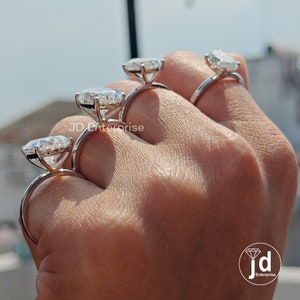 Puede incluir: Tres anillos de compromiso de plata con grandes piedras preciosas redondas y transparentes. Los anillos est&aacute;n en la mano de una persona, con el anillo m&aacute;s grande en el dedo &iacute;ndice, el anillo del medio en el dedo medio y el anillo m&aacute;s peque&ntilde;o en el dedo anular.