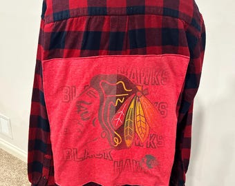 Może przedstawiać: Flanelowa koszula w kratę czerwoną i czarną z czerwoną naszywką z tyłu przedstawiającą logo Chicago Blackhawks i napis "Blackhawks".