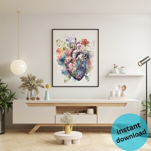 May include: A watercolor painting of a human heart with flowers growing from it. The heart is a light gray color with red veins and a blue background. The flowers are pink, red, yellow, and purple. The painting is framed in a black frame and is hanging on a white wall.