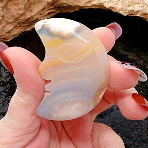 May include: A crescent moon shaped agate carving with white, yellow, and light blue banding. The agate is polished and smooth.