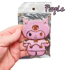 May include: A pink and gold metal character with a skull on its head and a pink and gold outfit. The character is in a plastic bag with the word "Purple" written on it.