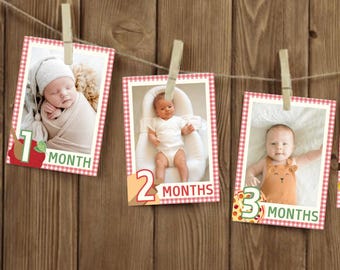 May include: A series of five baby photos, each clipped to a string with a wooden clothespin. Each photo is framed with a red and white checkered border and labeled with the baby's age in months, from one to five.