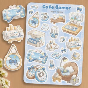 May include: A sheet of stickers with a cute gamer theme. The stickers feature gaming consoles, accessories, and bunny characters in pastel blue and beige. The text "Cute Gamer" is at the top.