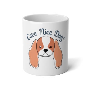 Pode incluir: Caneca de cerâmica branca com um cão de desenho animado Cavalier King Charles Spaniel com pelo marrom e branco, piscando. O texto "Cava Nice Day" é impresso em azul na caneca.