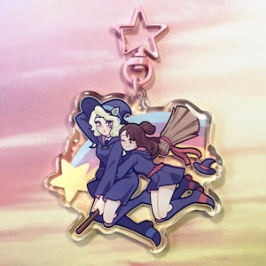 Può includere: Un portachiavi in acrilico trasparente con due streghe che volano su una scopa. Le streghe indossano abiti blu e viola con stelle e un arcobaleno sullo sfondo.