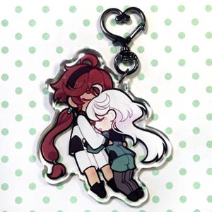 Può includere: Un portachiavi in acrilico trasparente con un'illustrazione a cartoni animati di due figure che si abbracciano. Una figura ha i capelli rossi, l'altra ha i capelli bianchi. Il portachiavi ha una chiusura nera a forma di cuore.