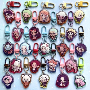 May include: Collection of colorful acrylic keychains featuring various anime characters. Each keychain has a unique design with vibrant colors and attached to a metal clasp. The keychains are arranged in rows, showcasing a variety of character designs.