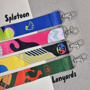 Könnte beinhalten: Vier bunte Lanyards mit verschiedenen Designs und silbernen Verschlüssen. Die Lanyards sind mit "Splatoon" und "Lanyards" beschriftet.