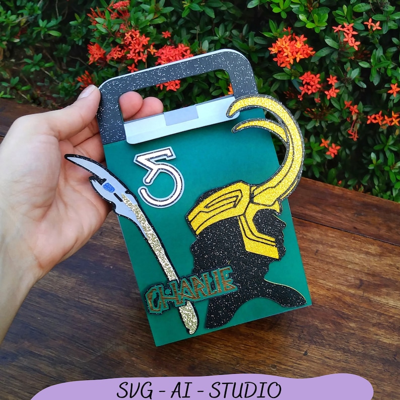 May include: A green cardstock party favor box with a gold glitter Loki silhouette, a gold glitter "Charlie" name tag, a gold glitter horn, and a white number "5" on the front.