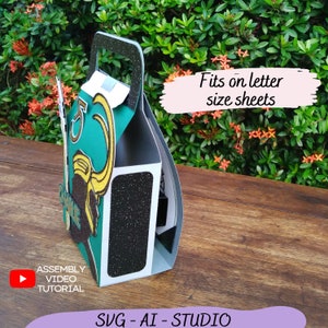 May include: A green, black, and gold paper party favor box with a character from the Marvel movie Thor. The box is designed to fit on letter-sized paper. The text "Assembly Video Tutorial" and "SVG - AI - STUDIO" are visible on the box.