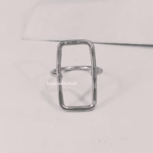 Pode incluir: Um anel de prata com formato retangular. O anel é feito de metal martelado e tem um acabamento texturizado.