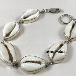 Peut inclure: Un bracelet en argent avec des coquillages de cauris blancs. Le bracelet a un fermoir à ressort et un anneau en argent.