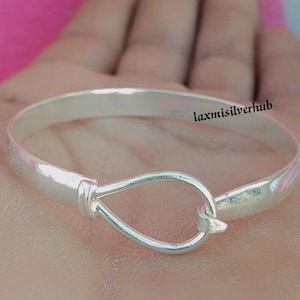 May include: A silver bangle bracelet with a teardrop-shaped clasp. The bracelet is smooth and shiny.