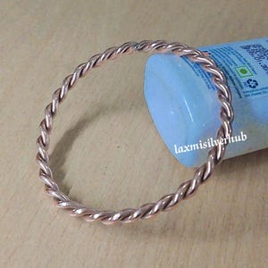 Puede incluir: Un brazalete de alambre de cobre con un diseño trenzado. El brazalete es de estilo simple y minimalista.