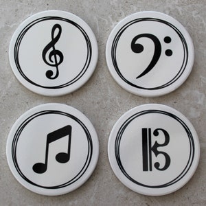 May include: Four white round coasters with black musical note symbols. The symbols are a treble clef, a bass clef, a whole note, and a quarter note.