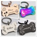 May include: Four different dog bone-shaped pet ID tags with engraved designs and names. The tags are in gold, rainbow, white, and black.