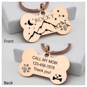 May include: Rose gold bone-shaped dog tag with a mountain and moon design on the front and the text "ROCKY" and the text "CALL MY MOM 123-456-7878 Thank you!" on the back.