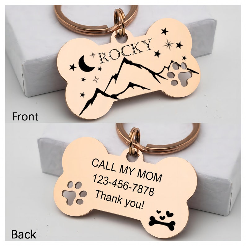 May include: Rose gold bone-shaped dog tag with a mountain and moon design on the front and the text "ROCKY" and the text "CALL MY MOM 123-456-7878 Thank you!" on the back.