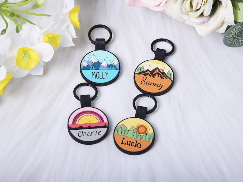 Puede incluir: Cuatro llaveros redondos con correas y anillos negros. Cada llavero presenta un dise&ntilde;o de paisaje diferente y un nombre: Molly, Sunny, Charlie y Lucki. Los dise&ntilde;os incluyen monta&ntilde;as, una puesta de sol y &aacute;rboles.