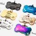 May include: A set of ten personalized dog bone-shaped tags in various colors, including black, gold, silver, blue, rose gold, and rainbow. Each tag features a different design and engraving, such as a palm tree, flowers, a rocket ship, and paw prints.