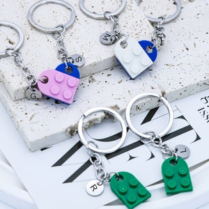 May include: Set of four silver keychains with heart-shaped charms. Each charm is made of plastic and features a different color combination of blue, white, pink, and green. The charms are shaped like Lego bricks and have the letters G, S, W, and L on the back.