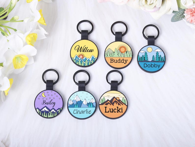 Puede incluir: Seis etiquetas redondas para mascotas con llaveros negros. Cada etiqueta presenta un dise&ntilde;o de paisaje diferente y un nombre: Willow, Buddy, Dobby, Bailey, Charlie y Lucki. Las etiquetas tienen un tema colorido de monta&ntilde;a y naturaleza.