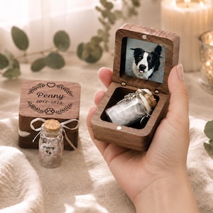 Pode incluir: Uma caixa de recorda&ccedil;&atilde;o em madeira escura com tampa articulada contendo um pequeno frasco de vidro. O interior da tampa exibe a foto de um c&atilde;o preto e branco. Uma caixa fechada a condizer apresenta a grava&ccedil;&atilde;o Penny 2012-2023 com uma pata.