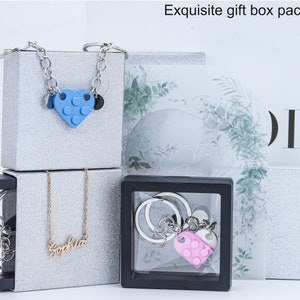 May include: Three gift boxes with jewelry inside. The top box has a silver chain necklace with a blue heart-shaped charm. The middle box has a silver chain necklace with a gold nameplate that says "Sophia". The bottom box has a silver keychain with a pink heart-shaped charm.